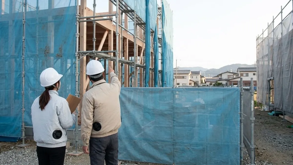 建築中の住宅の前で、スタッフが現場監督から説明を受けている様子